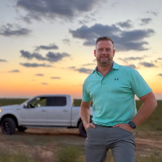 Joshua R. Barron standing in a West Texas field at sunset, hands on hips, his pickup behind him on the turnrow.